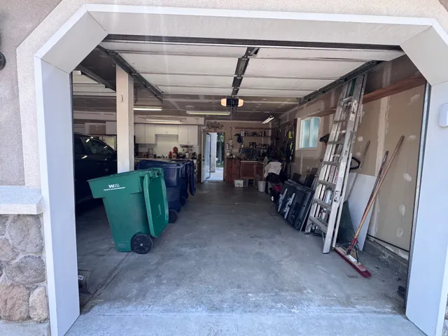 Garage interior featuring concrete flooring, exposed ceiling joists, and a rear utility area with built-in cabinetry and a window