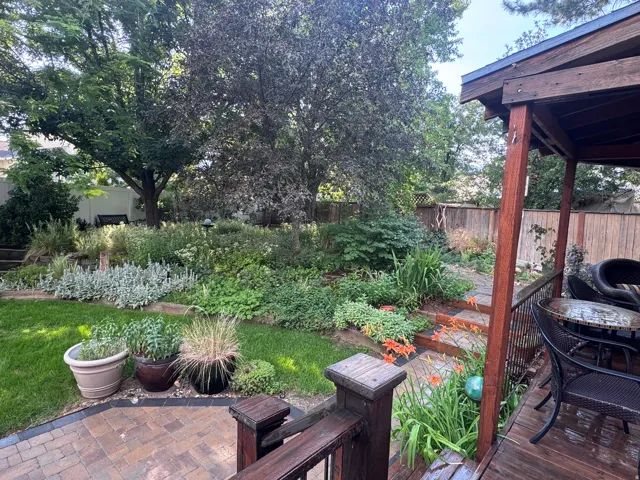 Expansive backyard featuring a wood-finish deck with built-in railing, a paver patio, mature trees, and layered landscaping