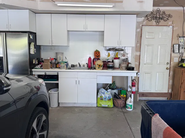 Garage utility area featuring white cabinetry, a stainless steel refrigerator, white tile backsplash, and a utility sink