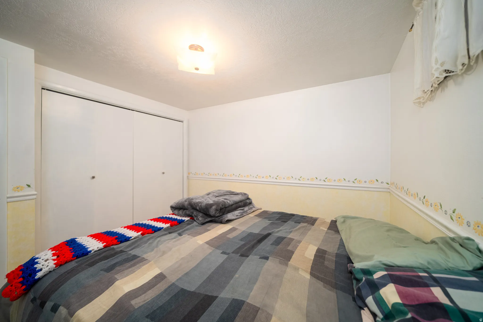 Spacious room featuring a wide closet with bi-fold doors, overhead flush-mount lighting, and light-toned walls with a decorative border