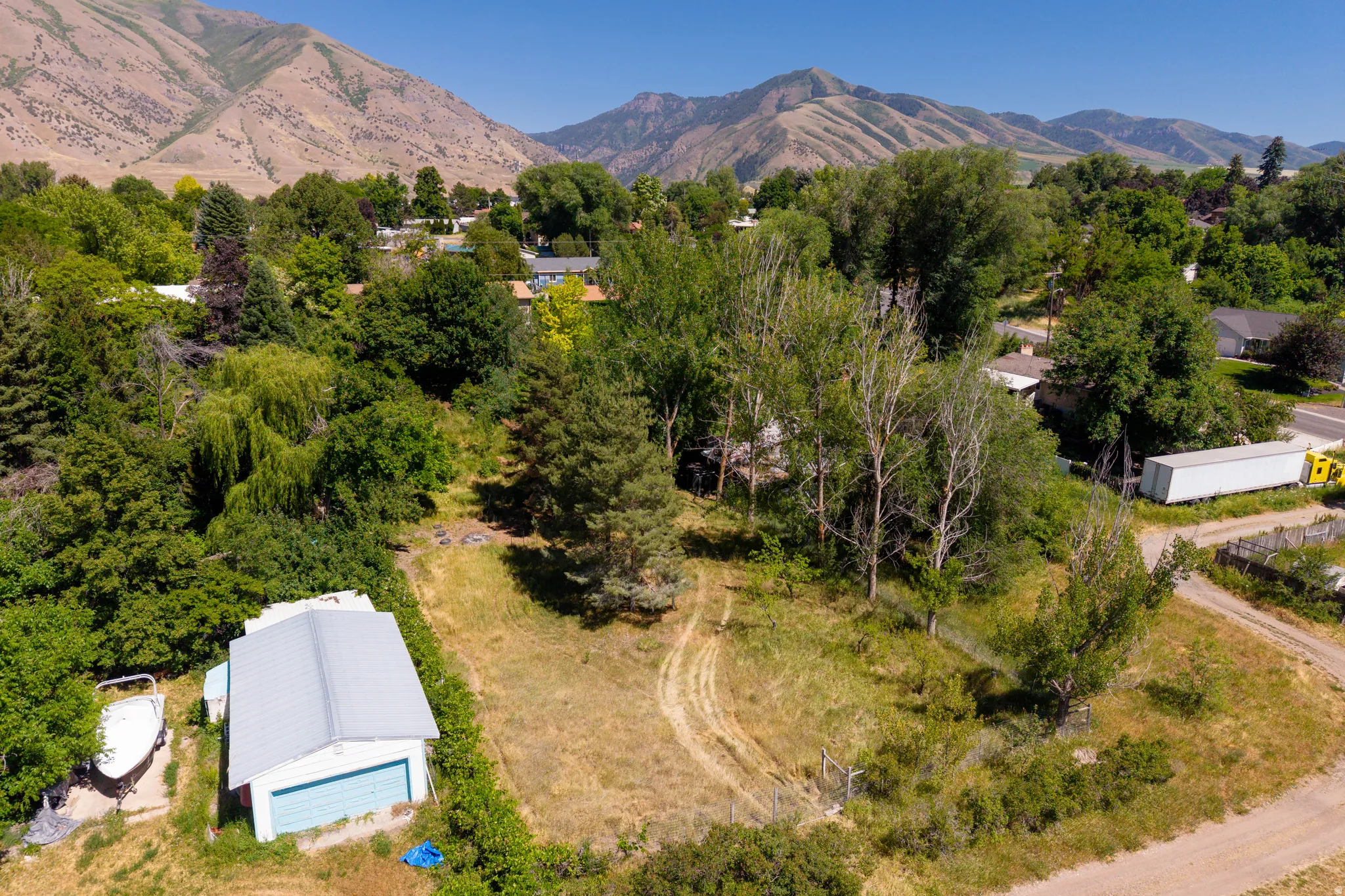 Expansive lot featuring mature trees, a detached garage with a light blue door, and a mountainous backdrop