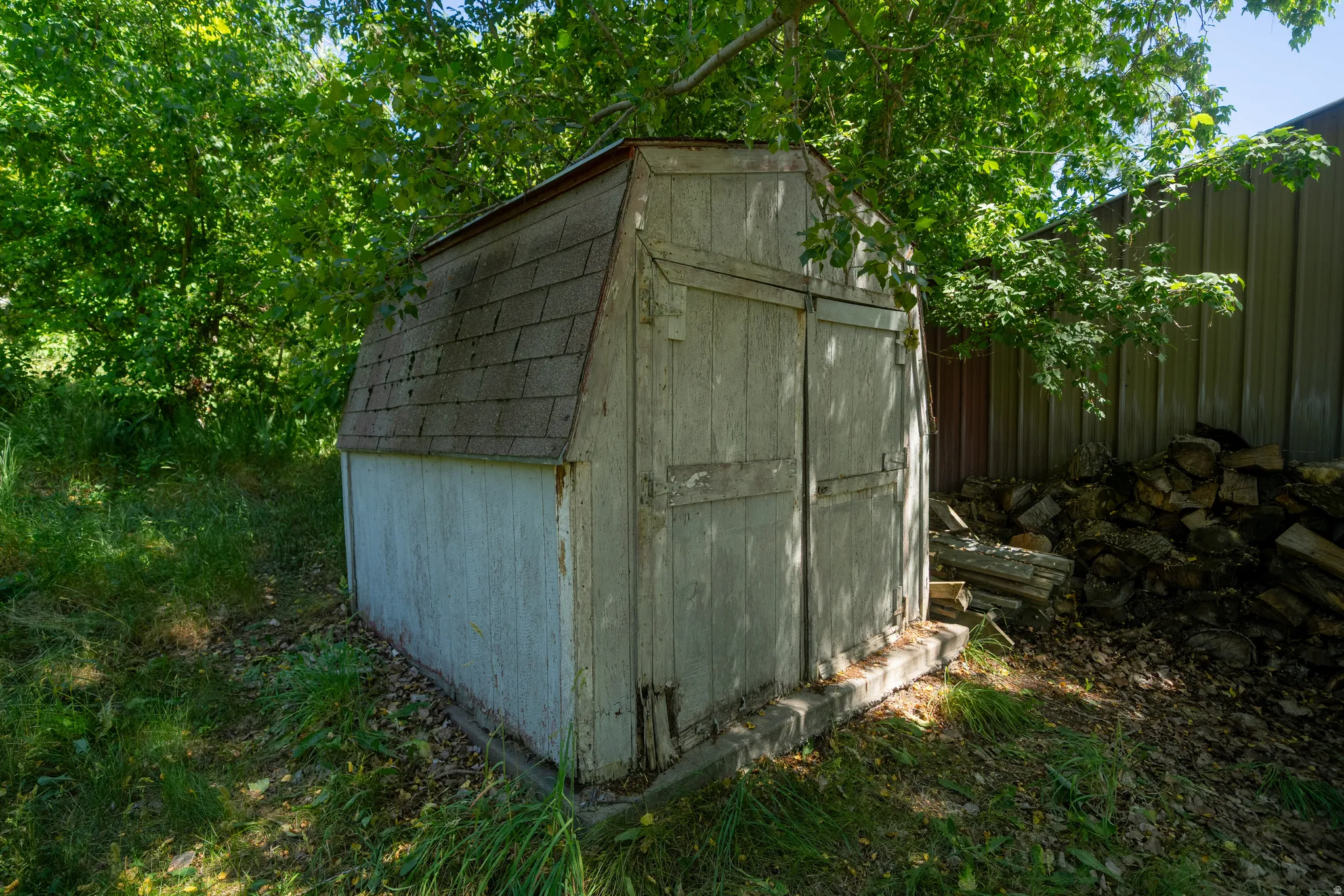 Wooden utility shed with a gambrel roof and asphalt shingles, set on a concrete foundation