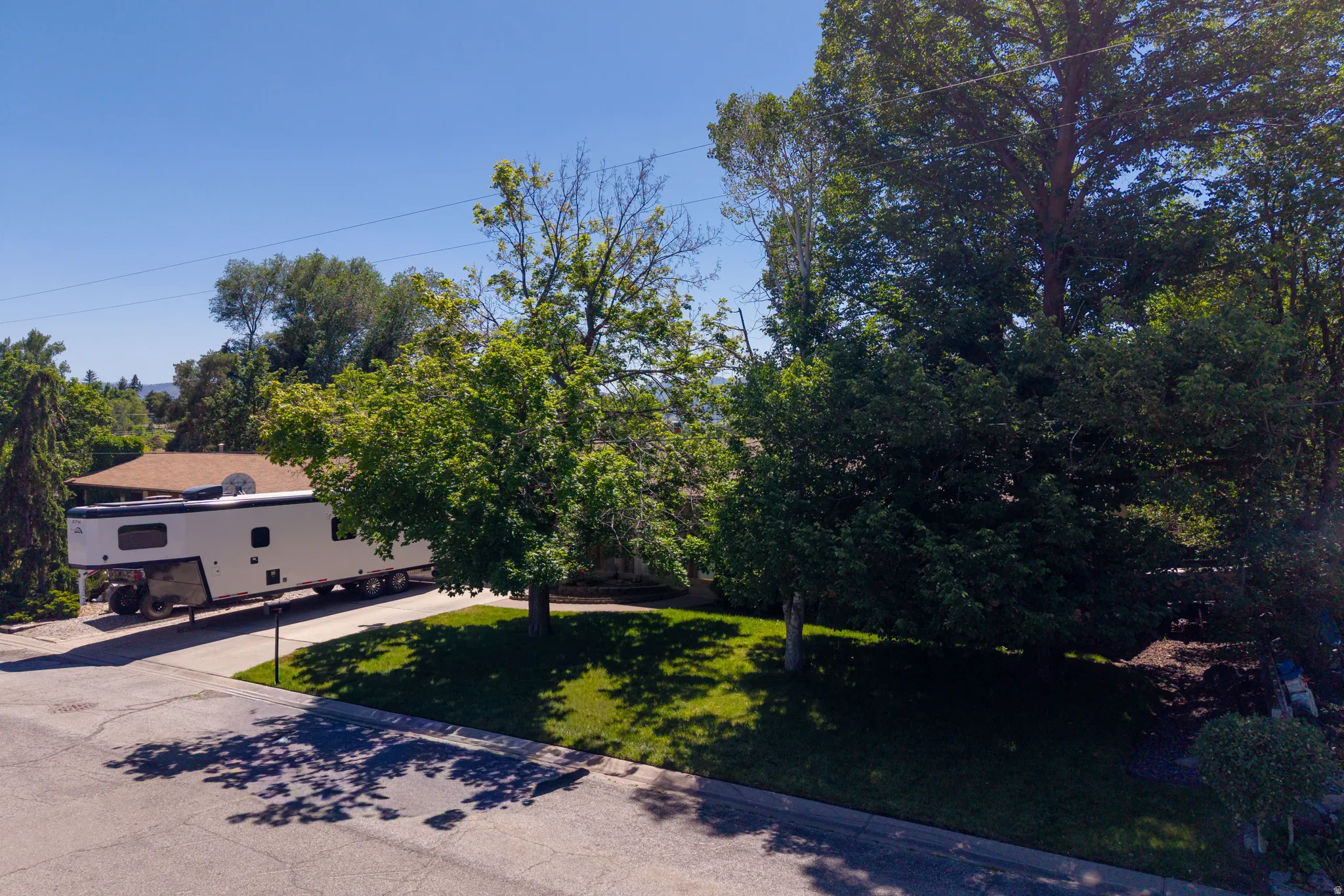 Paved driveway with ample parking space, bordered by mature trees and manicured lawn