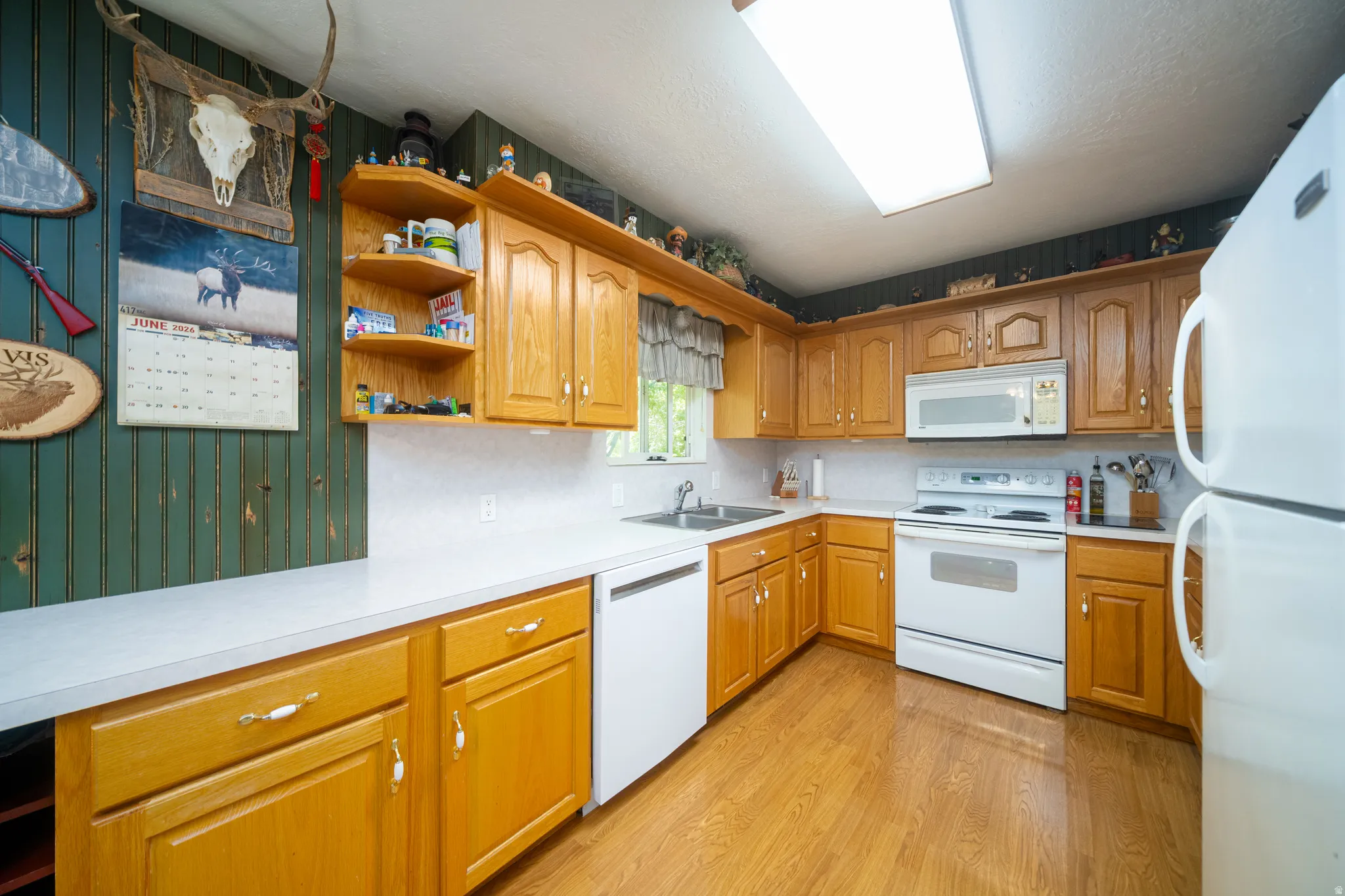 Kitchen featuring wood-finish flooring, wood cabinetry with gold-tone hardware, white countertops, and white appliances