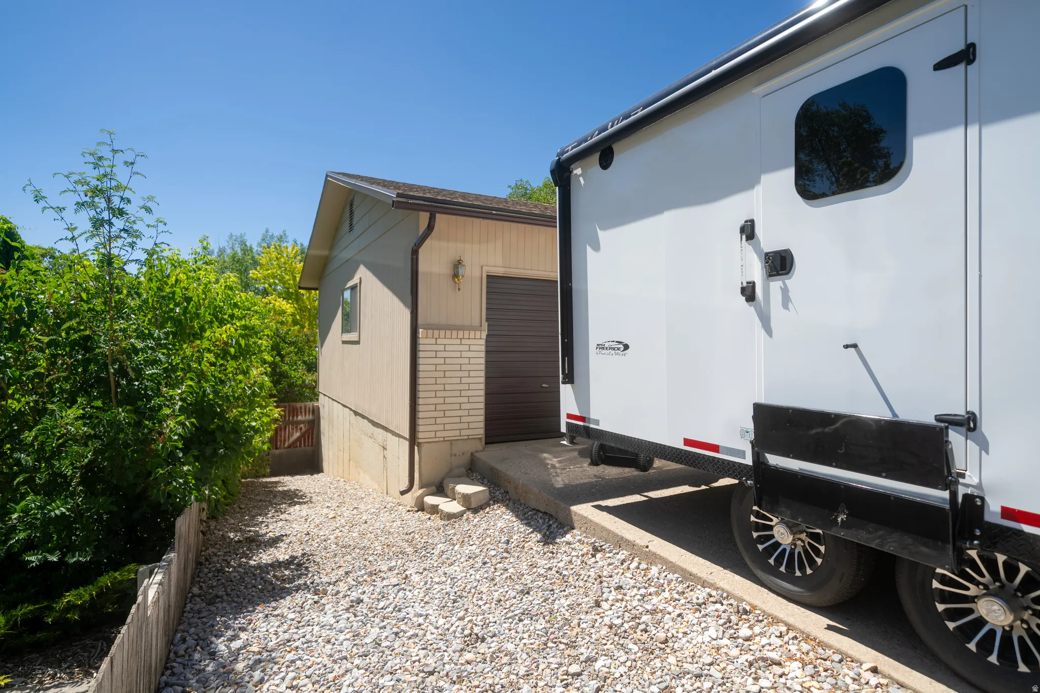 Detached accessory building with a brown garage door, light-toned siding, and a brick accent wall