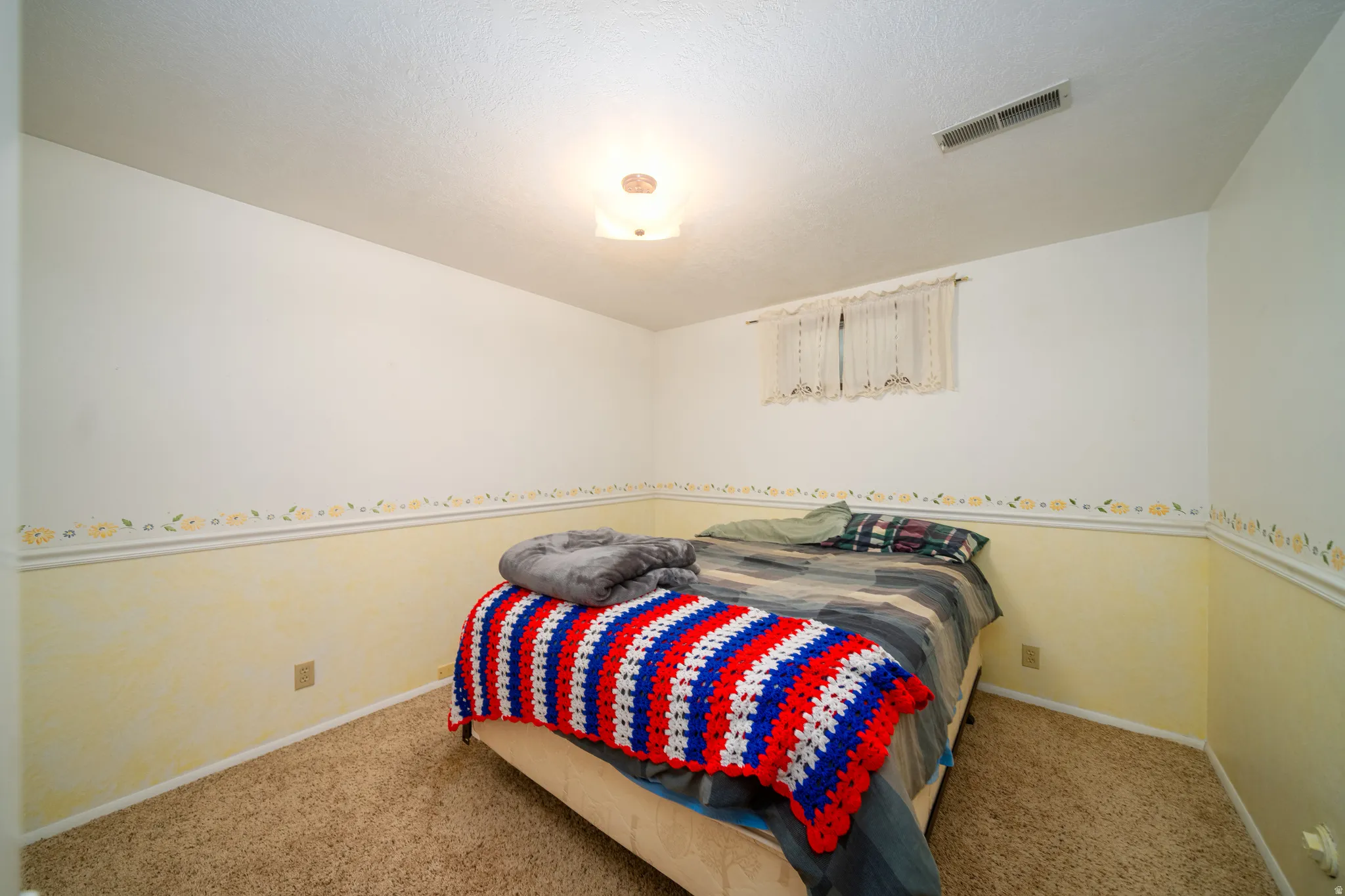 Carpeted room with a ceiling-mounted light fixture and a window with a sheer curtain
