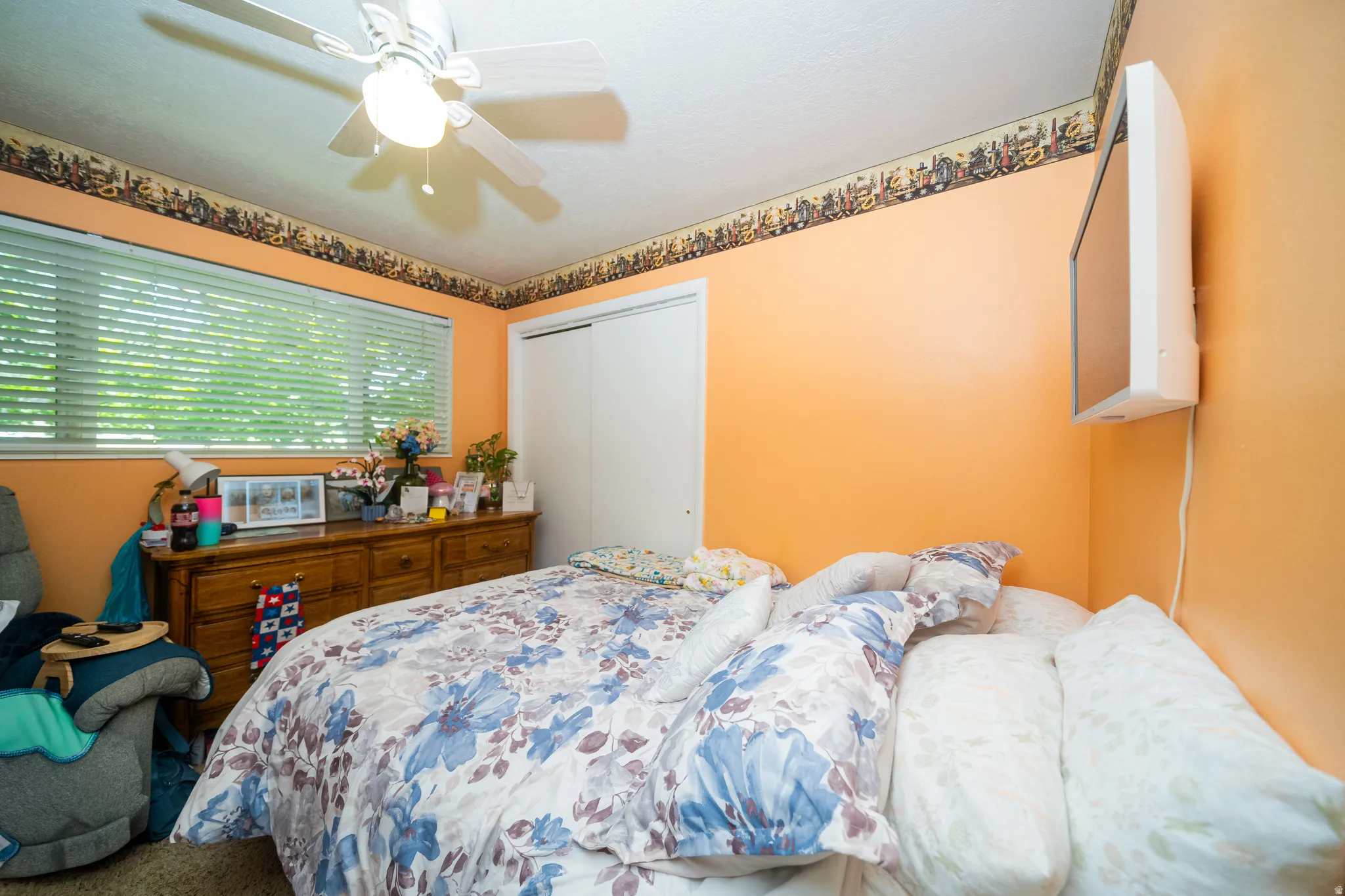 Room featuring a ceiling fan with integrated lighting, a wide window with horizontal blinds, and a built-in closet with sliding doors