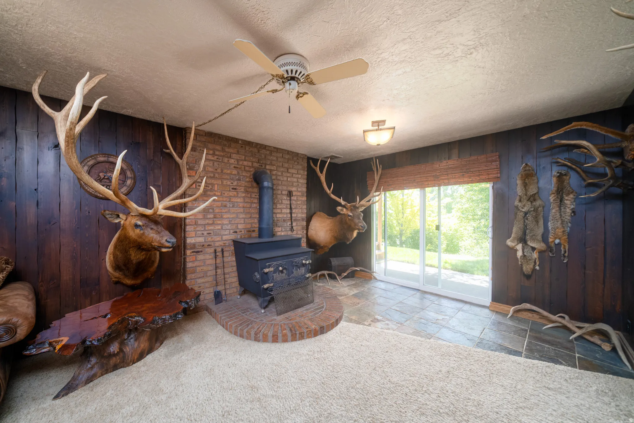 Spacious room featuring wood-paneled walls, a brick accent wall, and a central wood-burning stove with a brick hearth