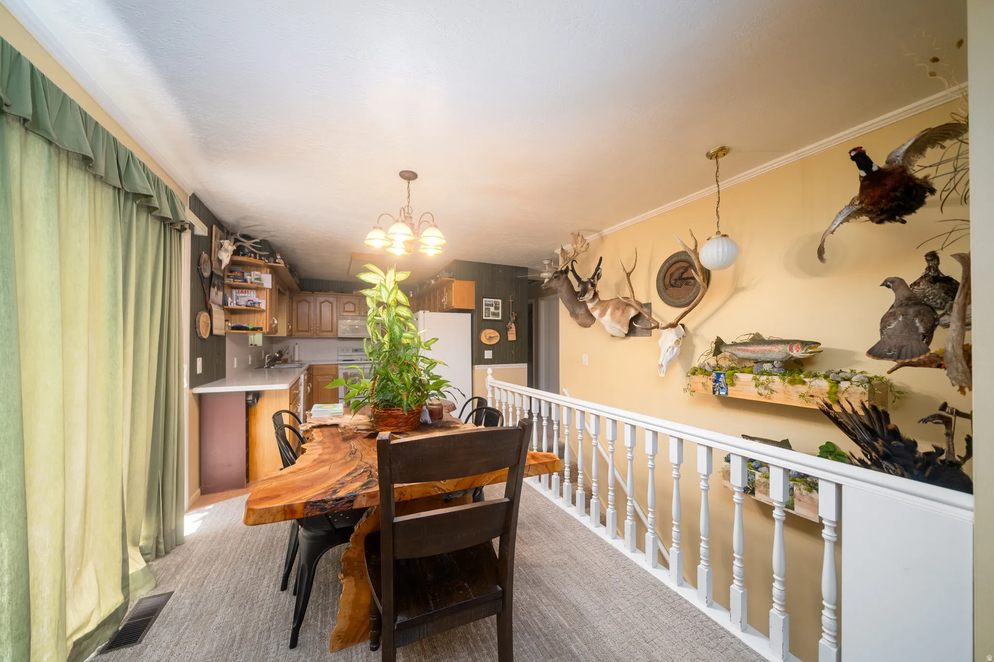 Open-concept kitchen and dining area featuring a distinct live-edge wood dining table, wood-finish cabinetry, a white railing, and track lighting
