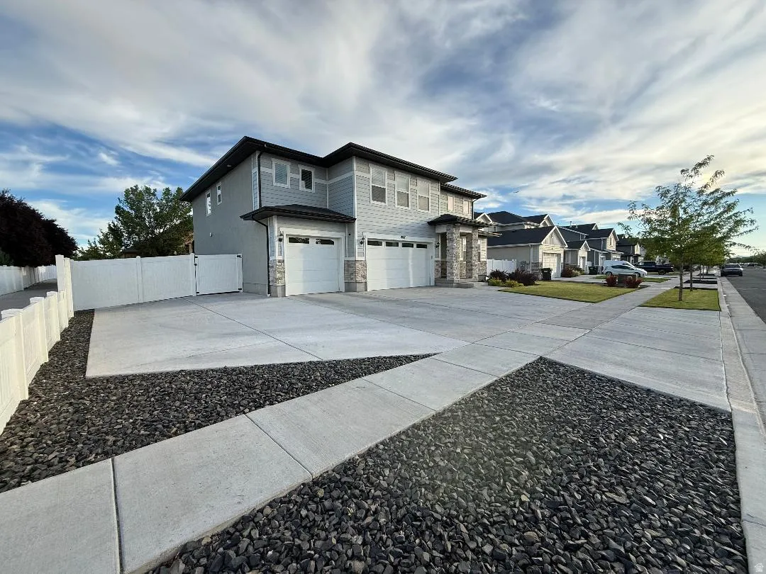 Two-story residence featuring light gray siding, stone accents, and a dark roof