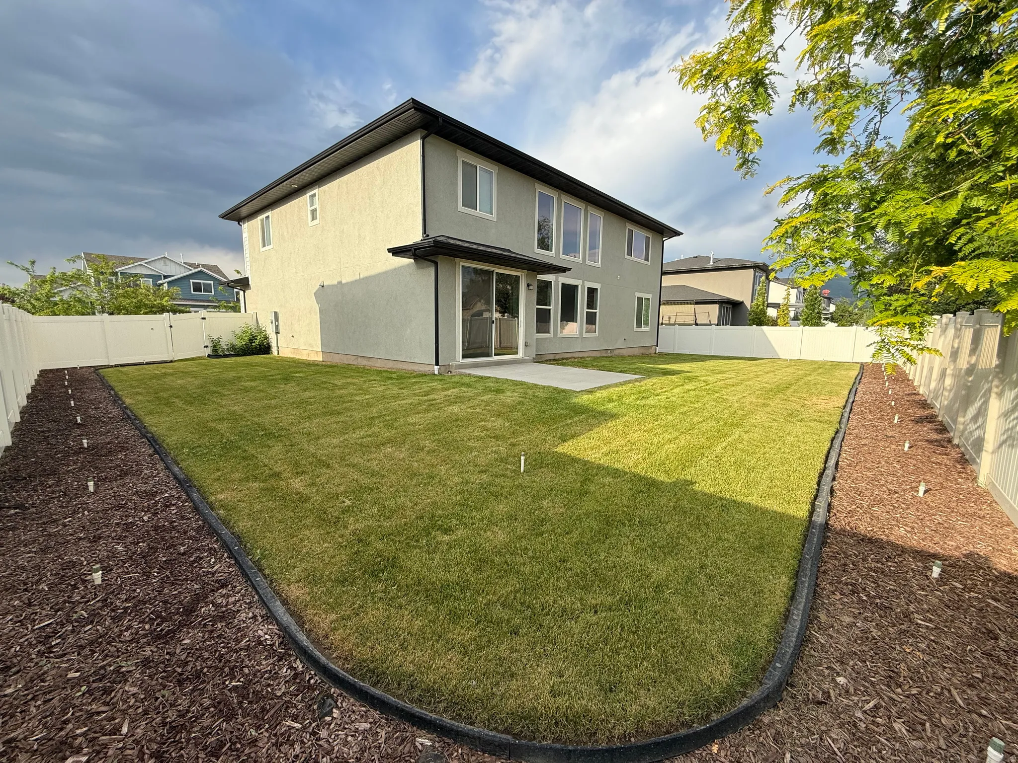 Expansive rear yard featuring a manicured lawn, concrete patio, and full vinyl fencing