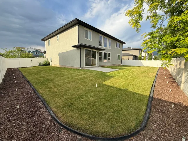 Expansive rear yard featuring a manicured lawn, concrete patio, and full vinyl fencing