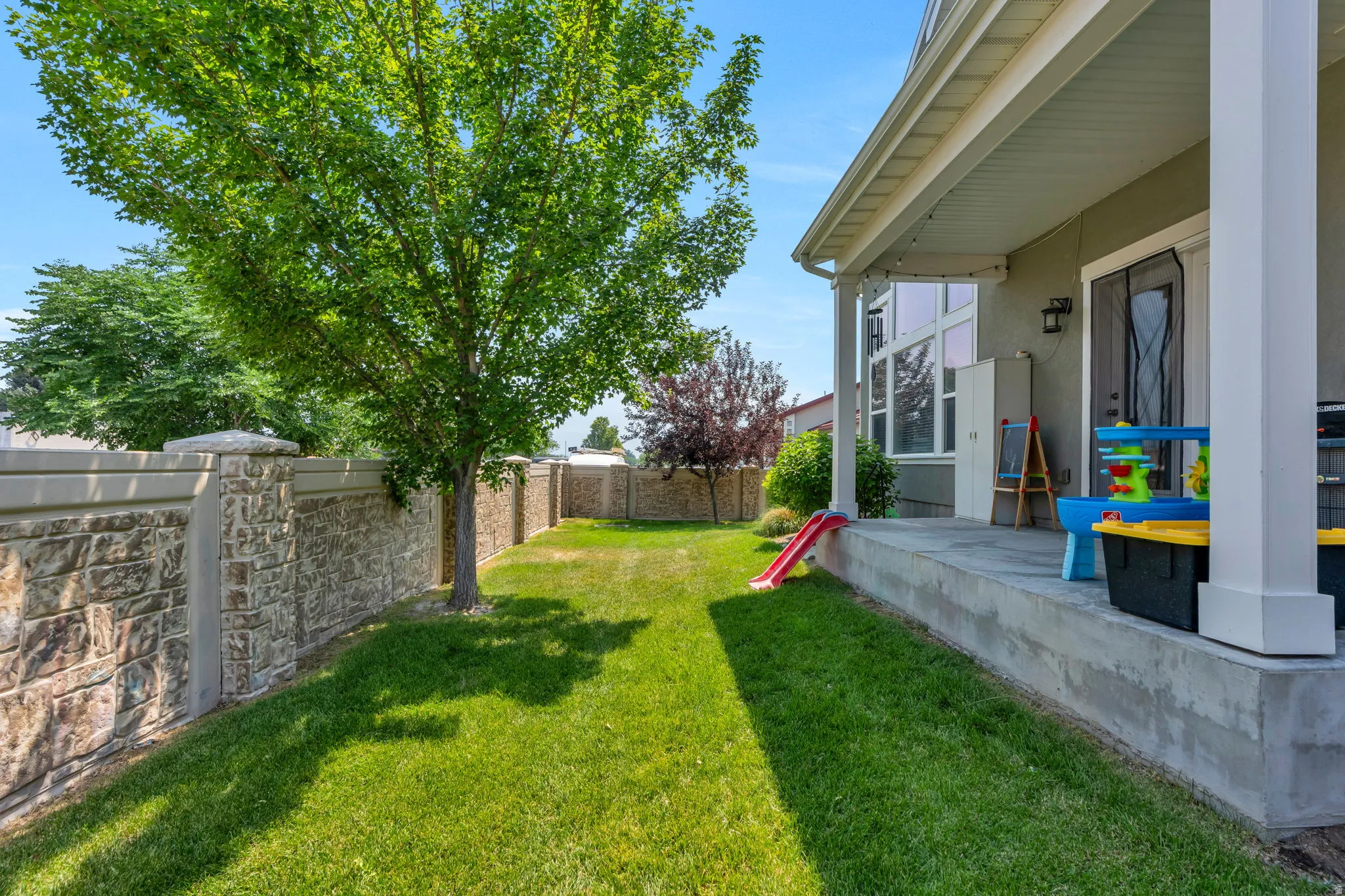 Expansive green lawn featuring mature trees and a stone-clad perimeter wall