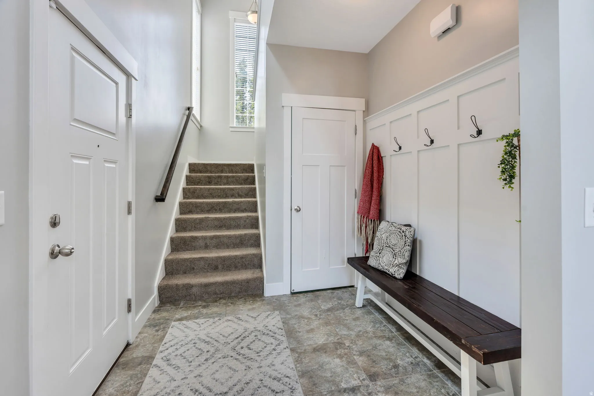 Entryway with white wainscoting with black coat hooks, and durable flooring