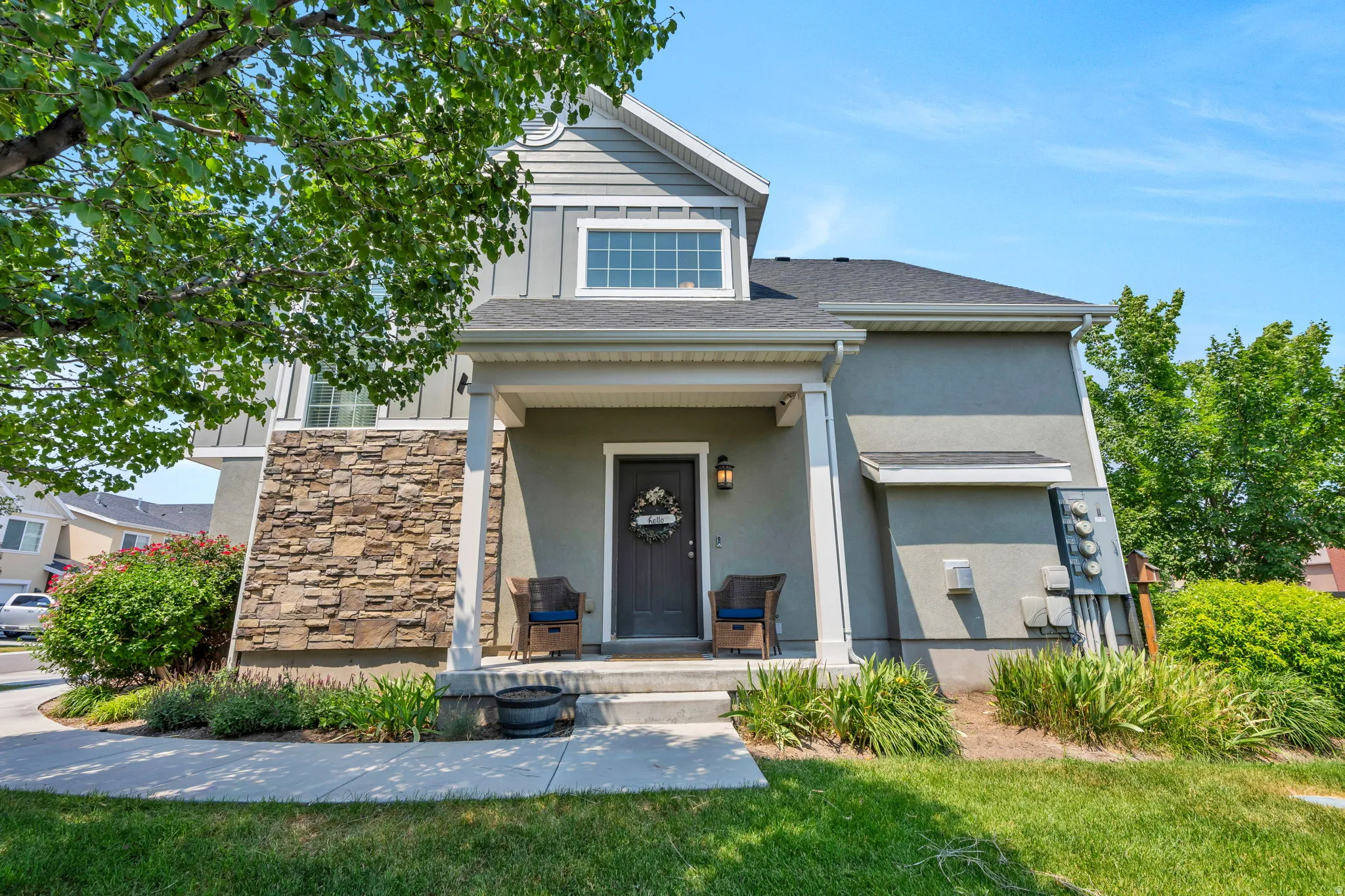 Contemporary home featuring a covered front porch, stone and siding exterior, a dark entry door, and manicured landscaping