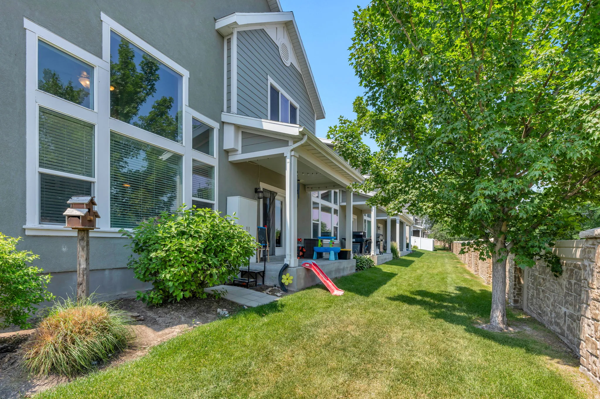 Rear exterior featuring large picture windows, a covered patio, and a stone retaining wall