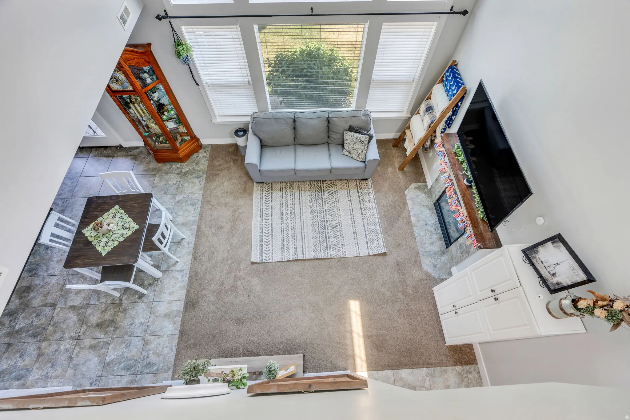Open-concept living area with high ceilings, large windows featuring blinds, a tiled dining area, and a carpeted living space with a fireplace