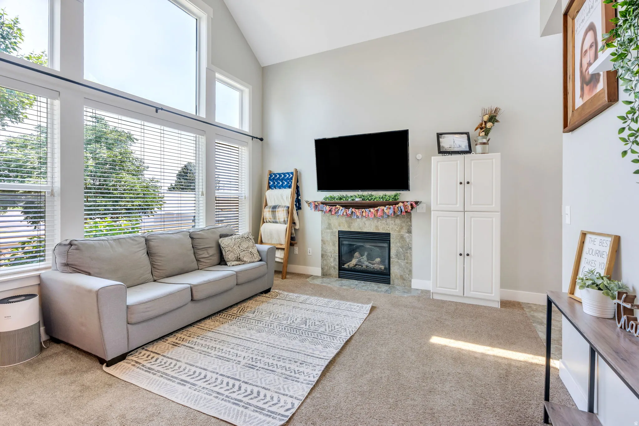 Living space featuring vaulted ceilings, a fireplace with stone surround, large picture windows, and built-in white cabinetry
