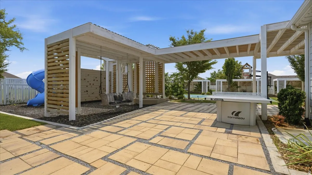 Expansive outdoor area featuring a patterned paver patio, a white pergola structure with wood slat accents, and a dedicated play space with a blue slide and swing set