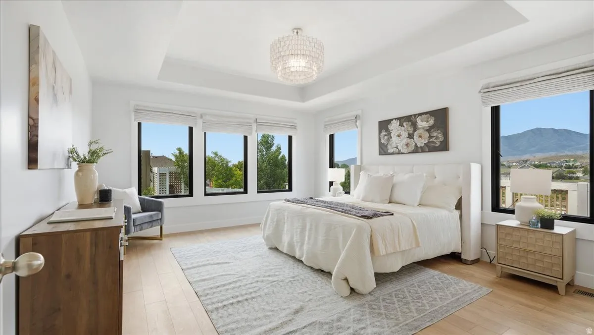 Expansive room featuring hardwood-style flooring, a tray ceiling with a decorative chandelier, and multiple large windows with mountain and neighborhood scenery