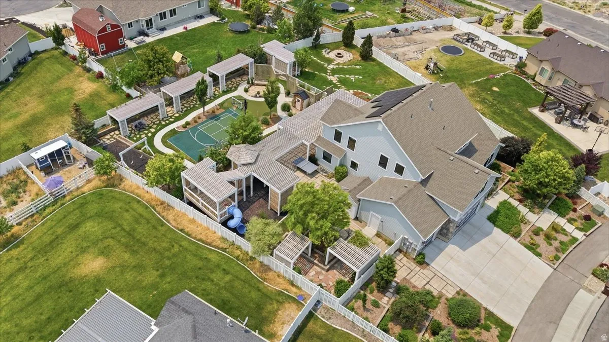 Expansive property featuring a multi-story residence with a gray exterior, a large paved driveway, a dedicated basketball court, multiple covered patio areas, and a substantial fenced yard