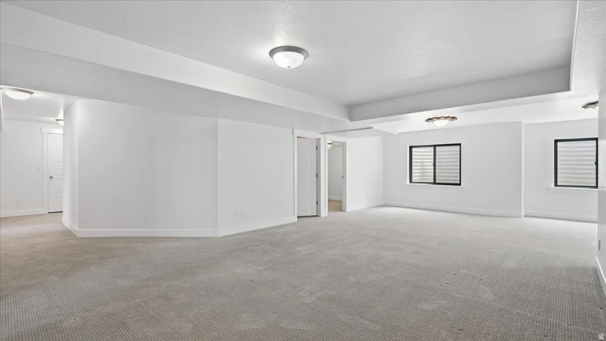Spacious room featuring light-colored carpet, white walls, and multiple windows with horizontal blinds