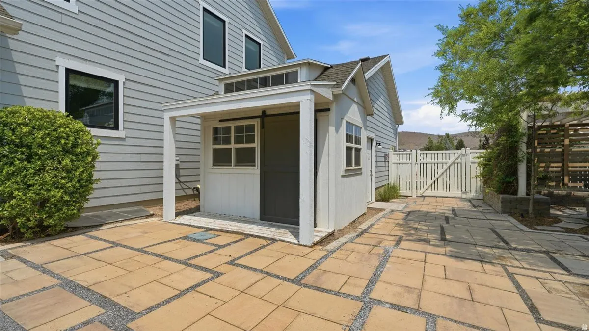 Patio area featuring square pavers and gravel accents, a detached shed with a sliding barn door, a white picket fence, and mature landscaping