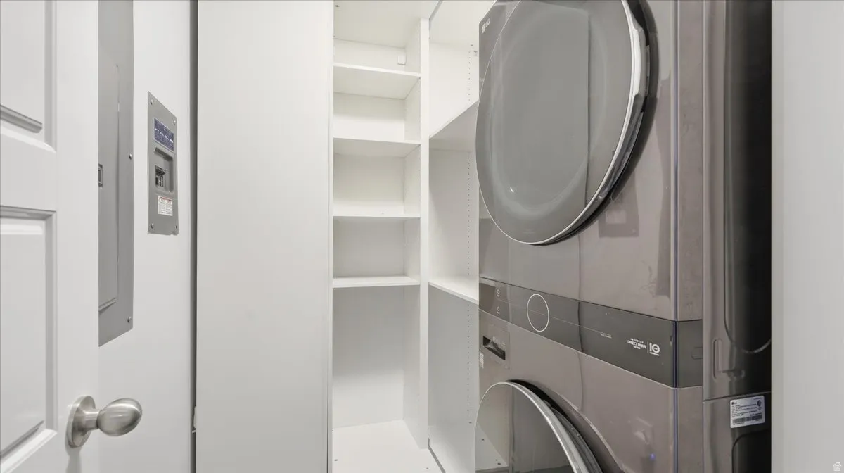 Dedicated utility area featuring a stacked washer and dryer unit, integrated shelving, and white wall finishes