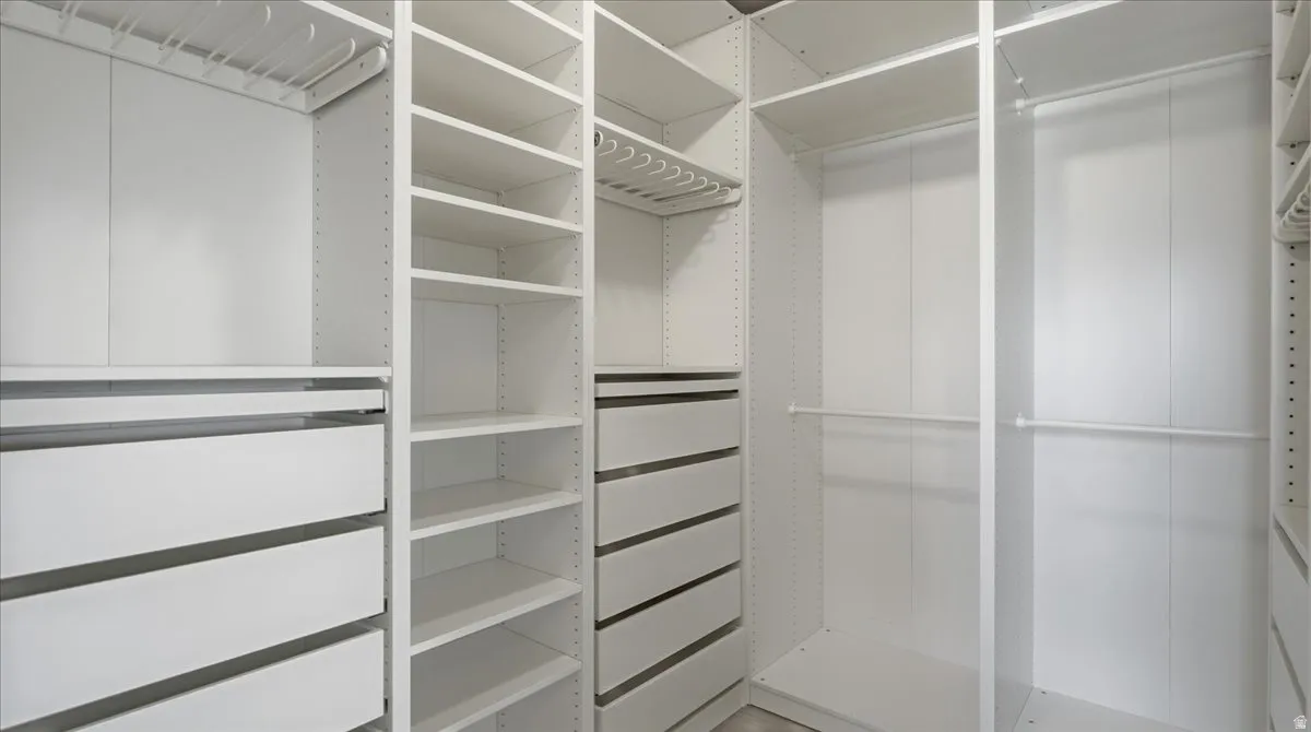 Custom closet system featuring white cabinetry, multiple hanging rods, integrated drawers, extensive shelving, and slide-out storage