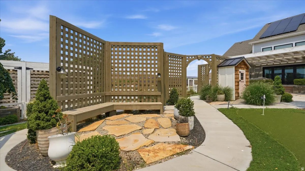 Curved lattice privacy screen with integrated bench seating, natural stone patio, and a dedicated putting green