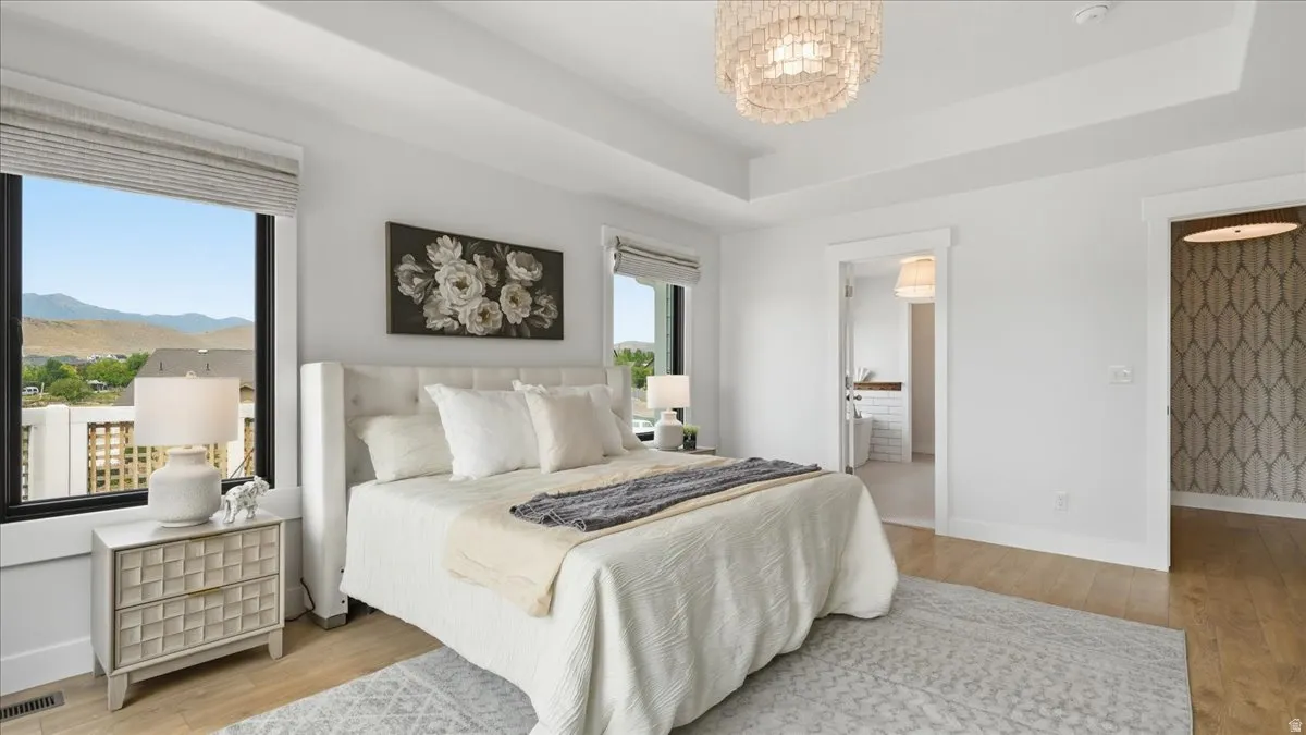 Spacious bedroom featuring light wood-finish flooring, a tray ceiling, and a contemporary beaded chandelier