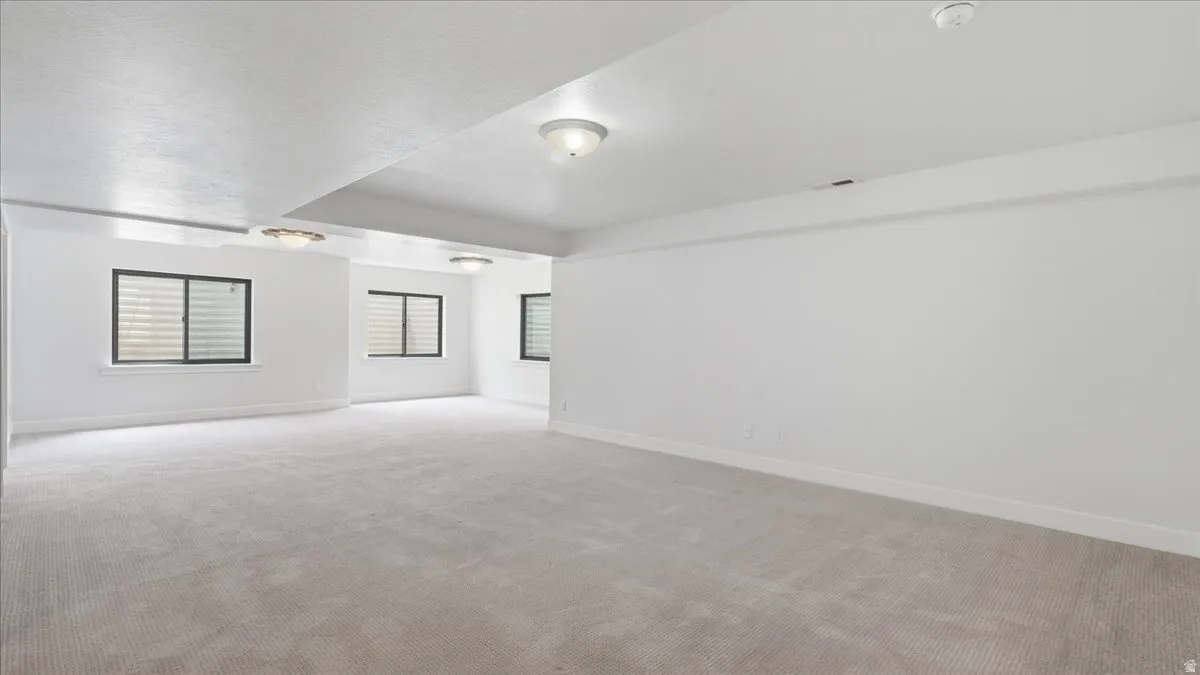 Spacious room featuring light-colored carpeting, multiple windows with horizontal blinds, and flush-mount ceiling lighting fixtures