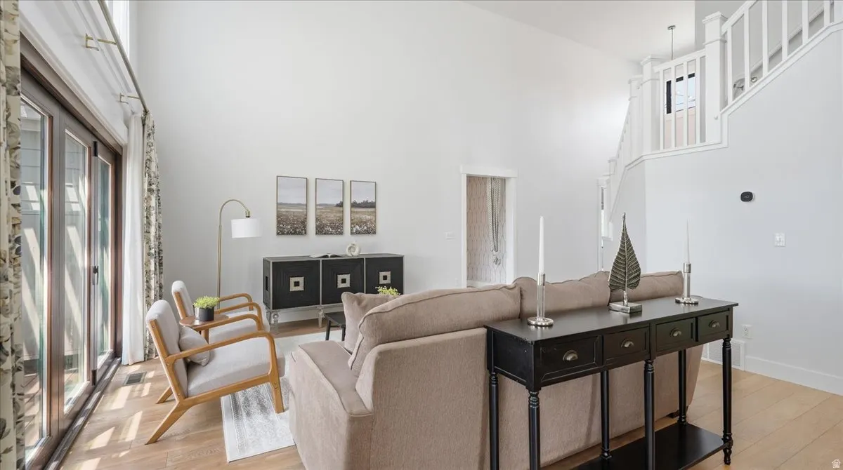 Vaulted ceilings enhance this living area featuring wood-finish flooring, a contemporary staircase with white balusters, and a wall of glass panel doors
