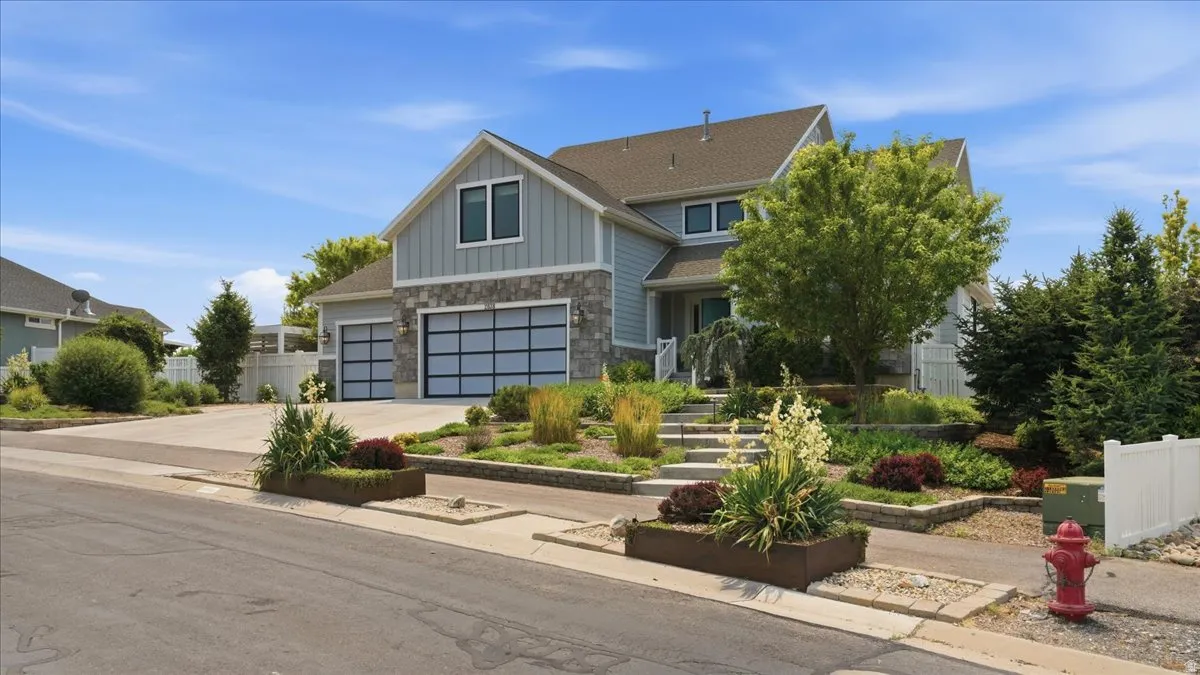 Contemporary residential exterior featuring light blue siding, stone accents, multiple gables, and a two-car garage with modern glass-paneled doors