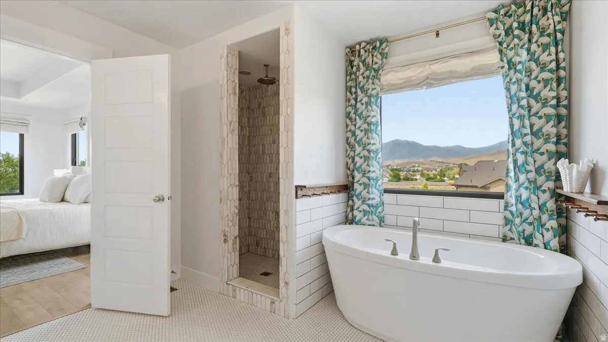 Freestanding soaking tub with brushed nickel fixtures, subway tile wainscoting, and a large picture window showcasing distant mountains