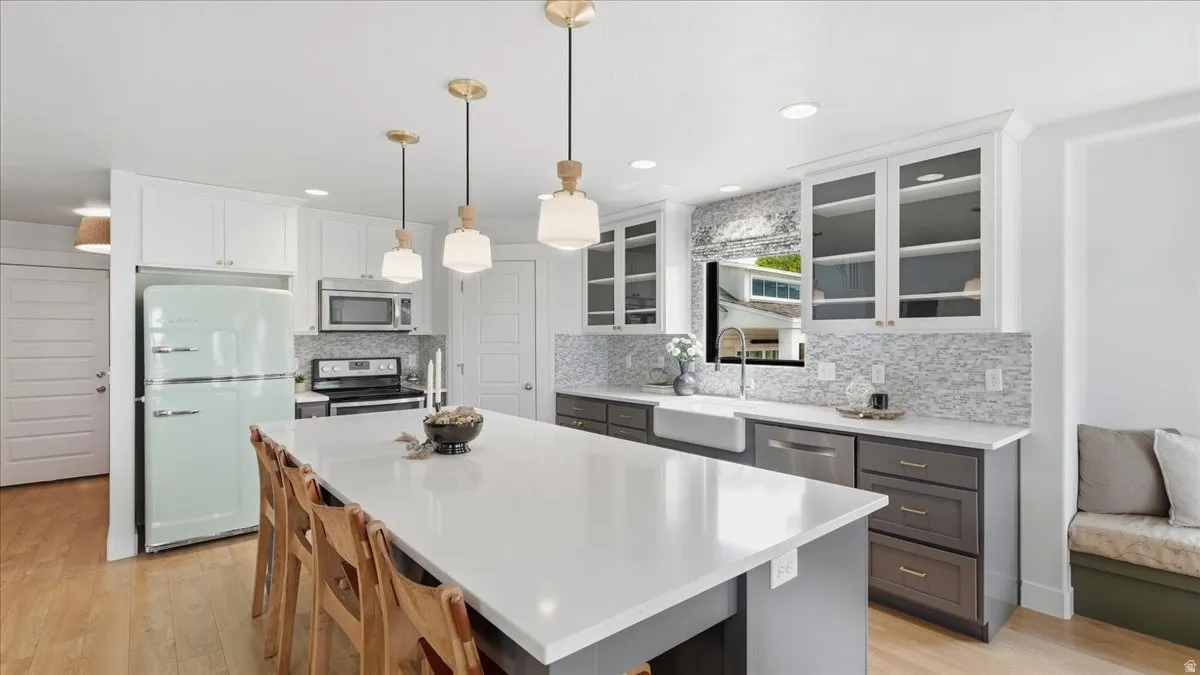 Kitchen featuring an expansive center island with seating, white shaker-style upper cabinetry, dark lower cabinetry, a farmhouse sink, and a patterned tile backsplash