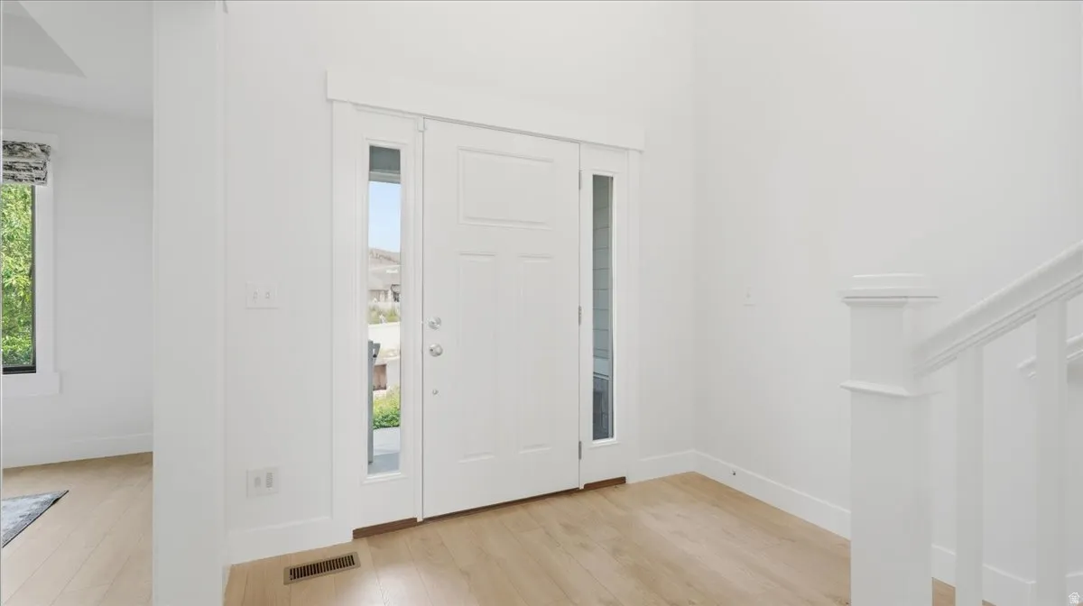 Entryway featuring a paneled door with glass side lites, light wood-finish flooring, white baseboards, and a white staircase railing