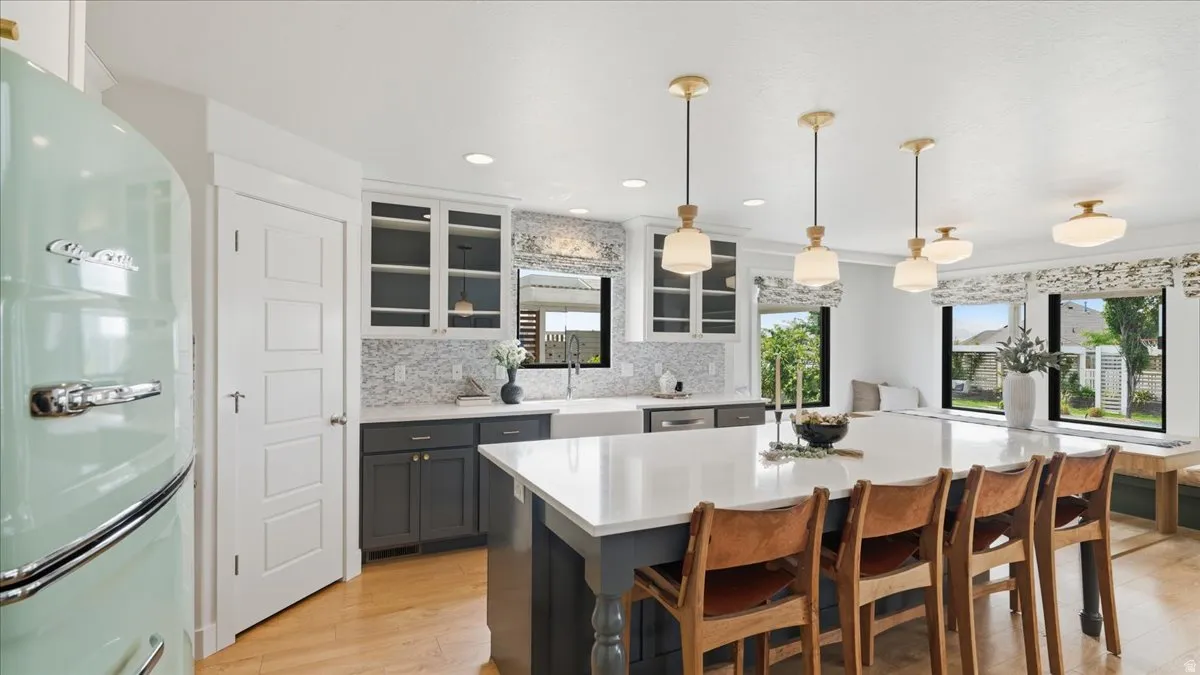Spacious kitchen featuring a large central island with seating, a patterned tile backsplash, white shaker-style upper cabinetry, dark lower cabinetry, and wood-finish flooring