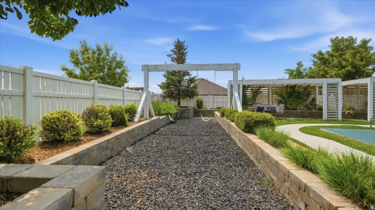 Expansive backyard featuring a gravel-filled activity area, a white picket fence, a swing structure, and a wood pergola with seating