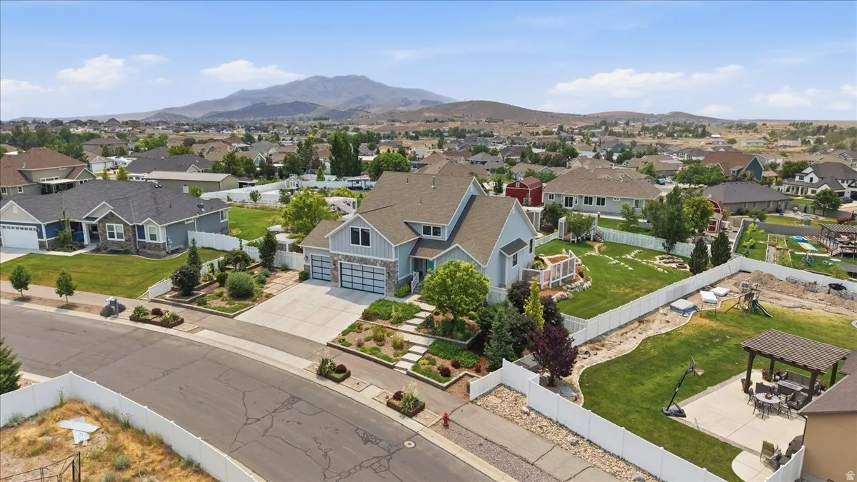 Contemporary home featuring a dual-tone exterior, attached three-car garage, mature landscaping, expansive backyard, and a mountain backdrop