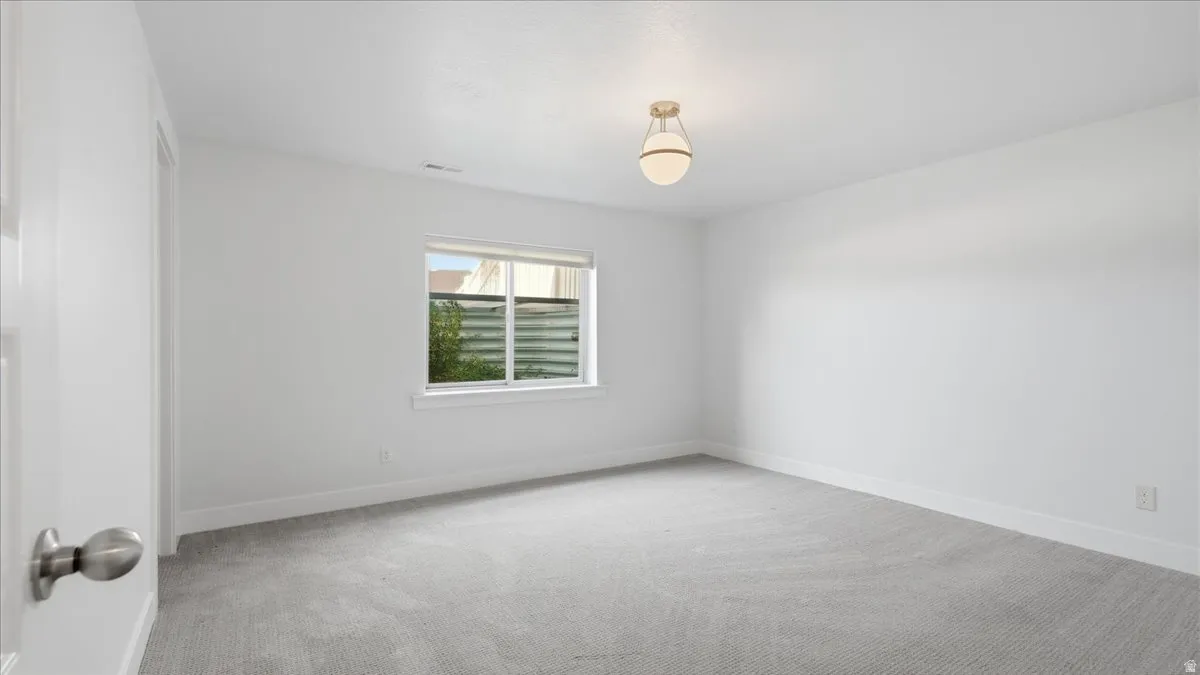 Spacious room featuring light gray carpet flooring, white painted walls, a flush-mount ceiling fixture, a window with horizontal blinds, and white trim molding