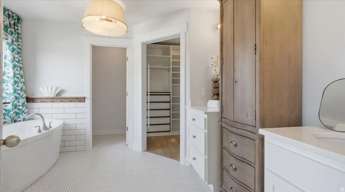 White hex tile flooring in a bathroom featuring a freestanding soaking tub, subway tile wainscoting, and an integrated wood-finish shelving unit
