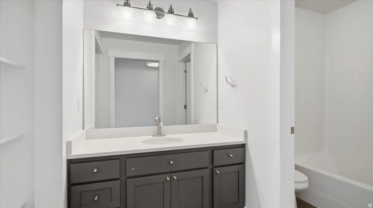 Bathroom vanity featuring a light-toned countertop, undermount sink, and dark cabinetry with brass hardware