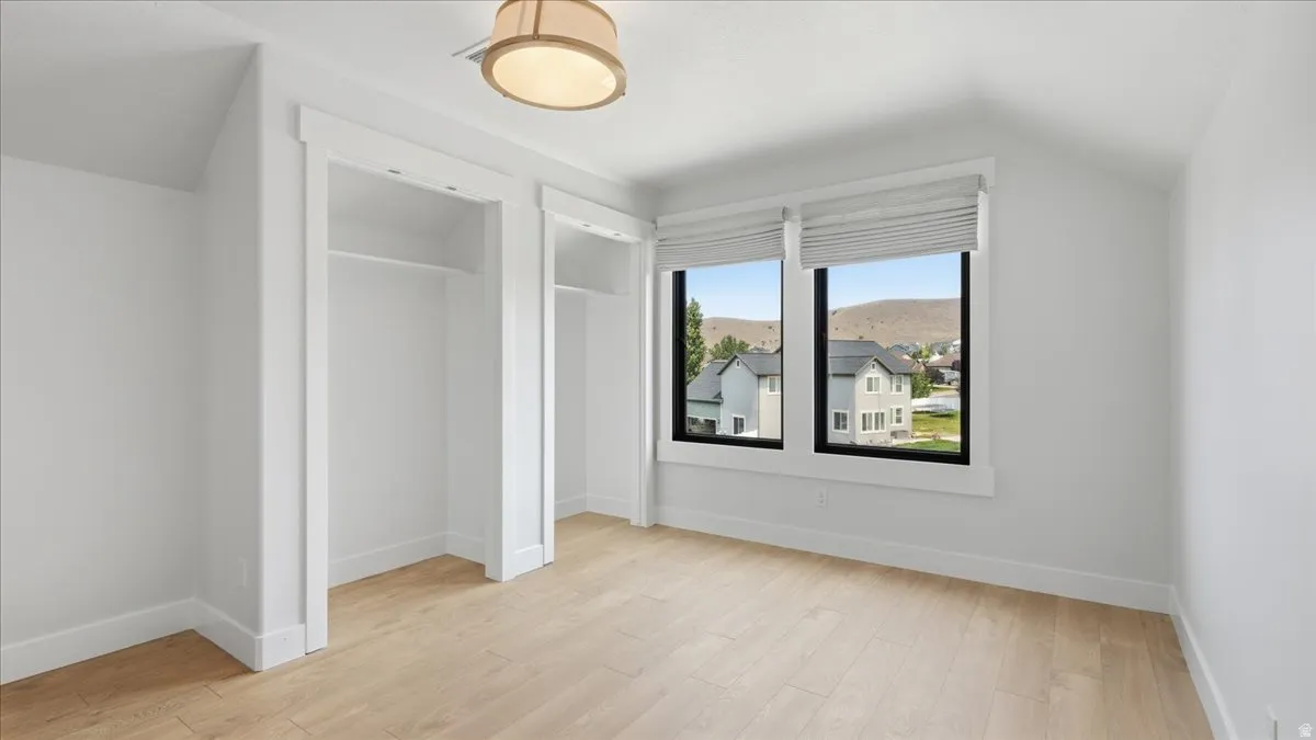 Light-filled room featuring wood-finish flooring, dual windows with Roman shades, two open closets with hanging rods, and a drum-style ceiling fixture