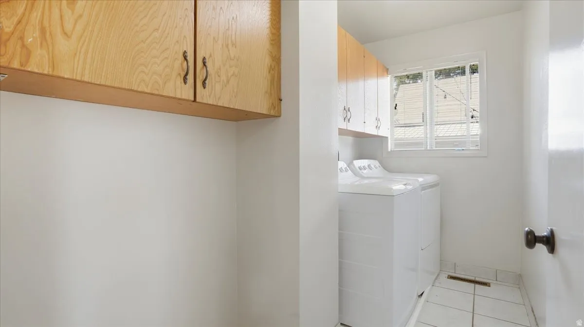 Laundry area featuring light wood-finish cabinetry with dark hardware and a white-framed window