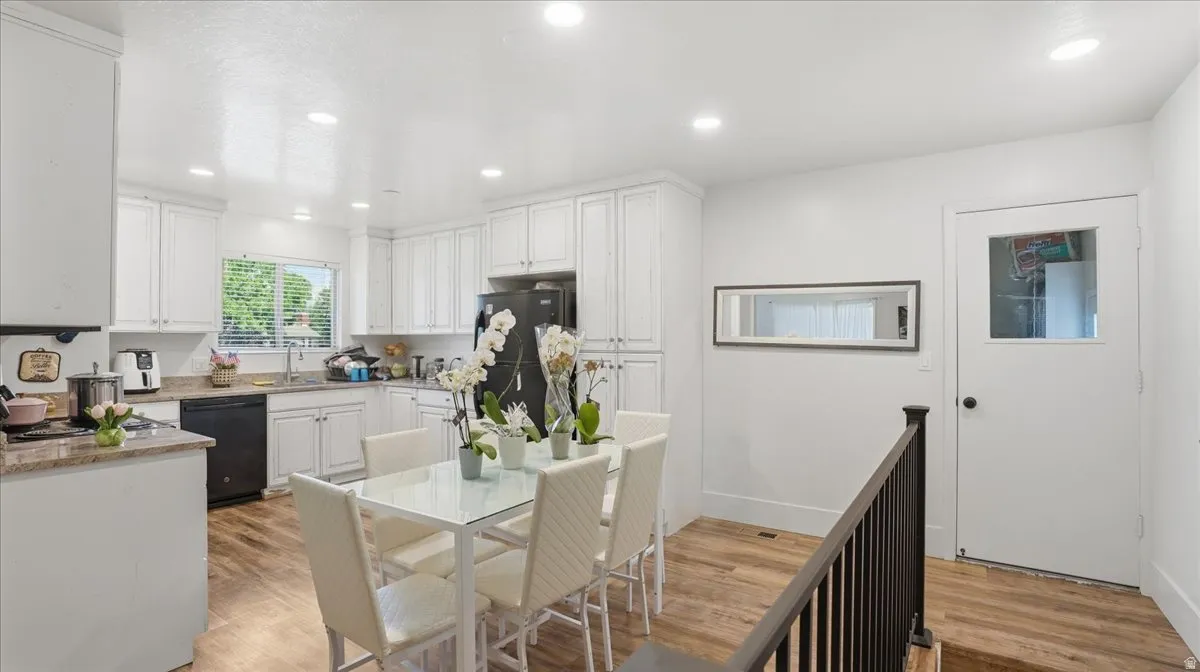 Open-concept kitchen and dining area featuring white cabinetry, black appliances, light-toned countertops, and wood-finish flooring