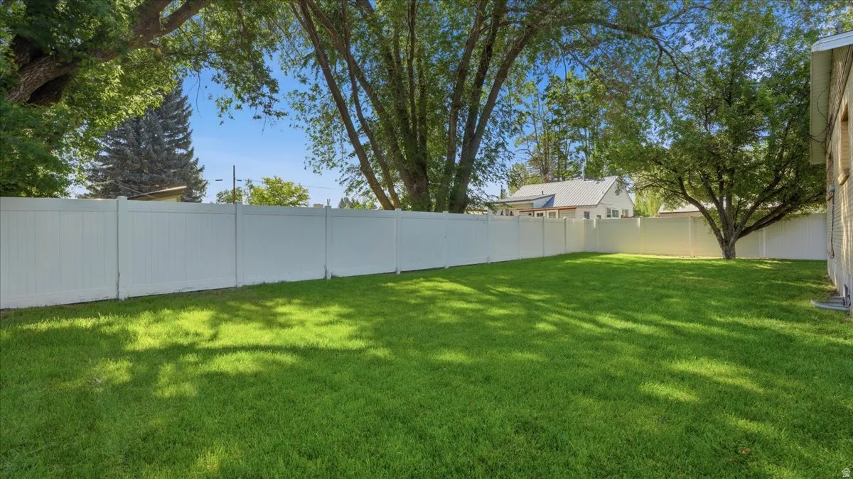 Expansive backyard featuring a manicured lawn, a full white vinyl privacy fence, and mature trees providing natural shade