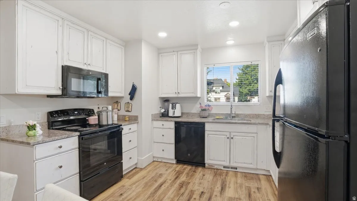 Kitchen featuring white cabinetry, black appliances, a double basin sink, light-toned countertops, and wood-finish flooring