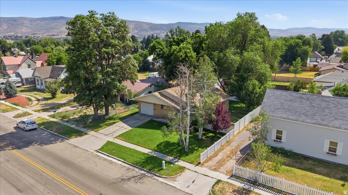 Single-story residence featuring an attached garage, well-maintained front lawn, mature trees, and a white picket fence bordering the property