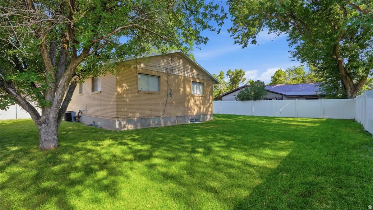 Spacious backyard featuring a lush green lawn, mature shade trees, a full privacy fence, and a brick exterior